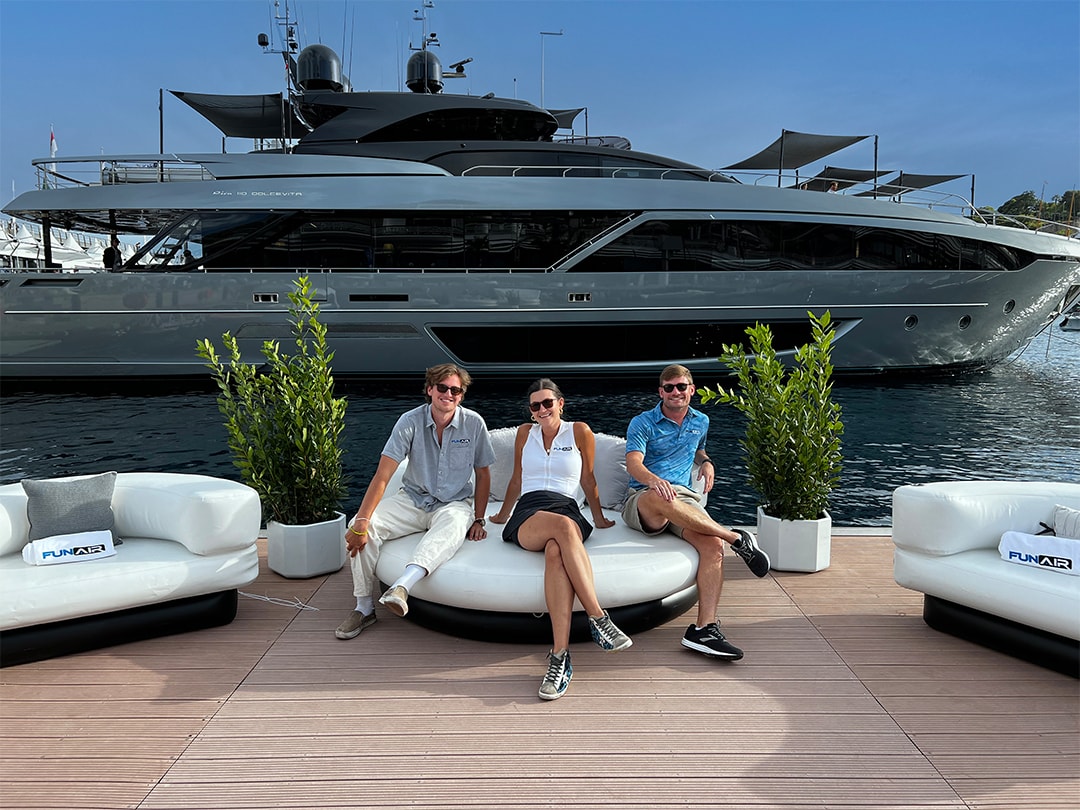 Three people sitting on the FunAir Club Chaise with a superyacht in the background