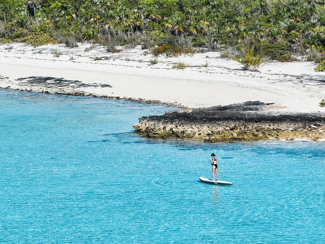 yacht charter guest on inflatable SUP near the shoreline of a tropical island