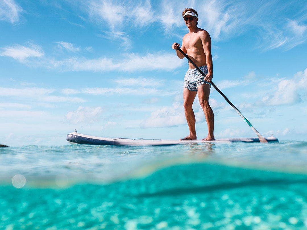 superyacht charter guest using an inflatable stand up paddle board on a clear blue sea