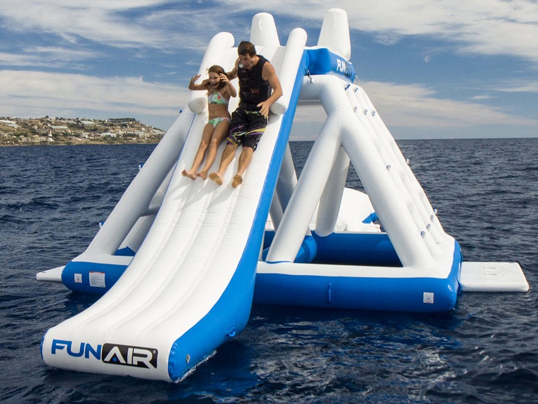 Man and girl sliding down the slide of a floating inflatable playground in the sea