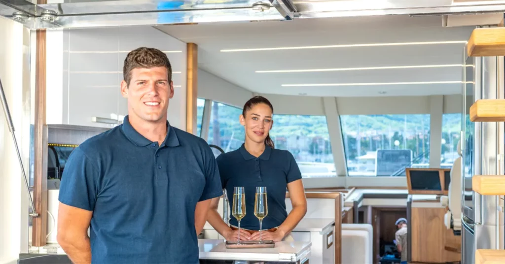Male and Female superyacht crew members welcoming charter guests on board with champagne