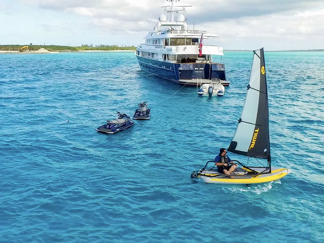 Charter guest sailing a Tiwal dinghy near a superyacht