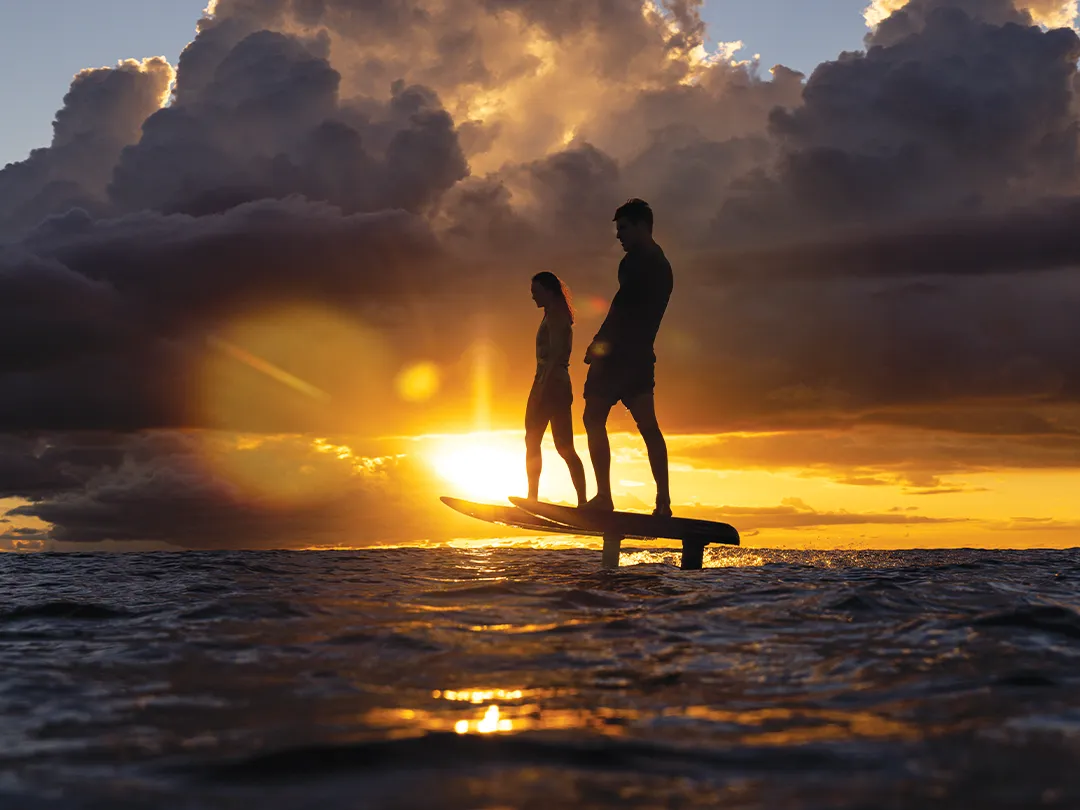 Charter yacht guests riding Fliteboards in front of a sunset