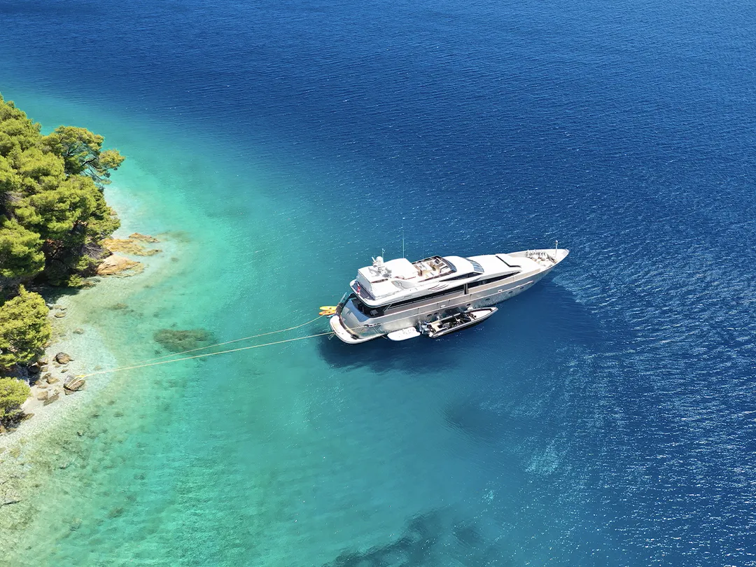 Overhead view of a charter yacht anchored off a rocky coastline
